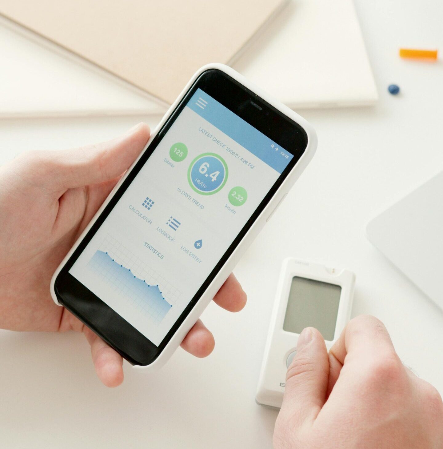 Close-up of hands using a smartphone app to monitor glucose levels with a digital glucometer on a table.