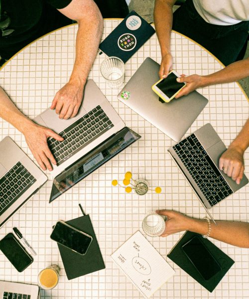 Top view of a team collaborating with laptops, phones, and notes in a modern office.